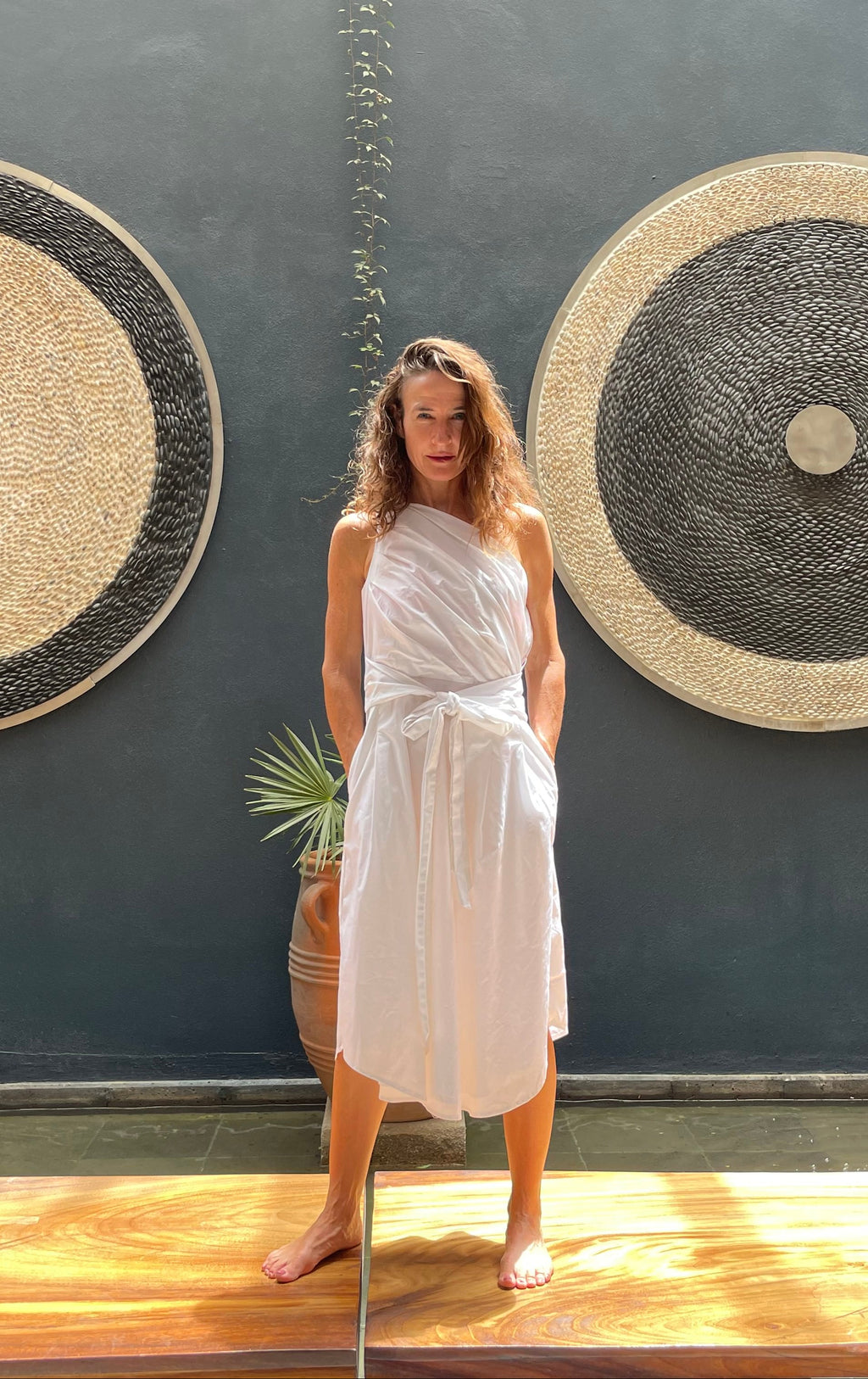 Woman in a white dress standing between two large circular wall art pieces against a dark wall.